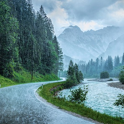 Blick auf eine kurvige Autostraße entlang eines Waldes und eines Flusses.