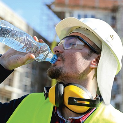 Ein Mann in Schutzausrüstung gegen Sonneneinstrahlung trinkt aus einer Wasserflasche.