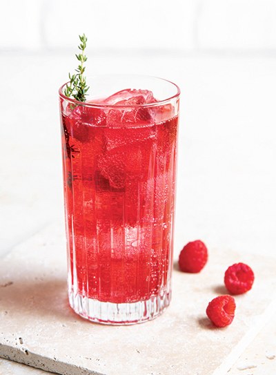  Ein Glas mit einem roten Drink und Himbeeren daneben.