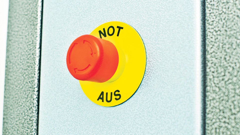 Not-Aus-Schalter – ein roter Pilzkopf auf gelbem Untergrund – mit der Beschriftung Not Aus auf dem gelben Untergrund.