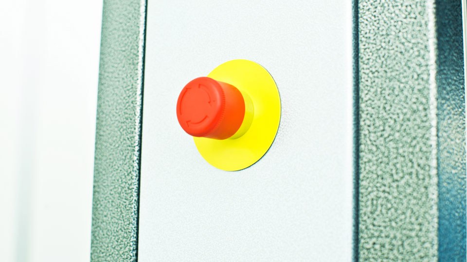Not-Aus-Schalter – ein roter Pilzkopf auf gelbem Untergrund – mit der Beschriftung Not Aus auf dem gelben Untergrund.