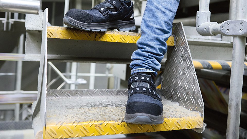 Eine Person wurde auf einer Treppe fotografiert. Zu sehen sind die Sicherheitsschuhe der Person.