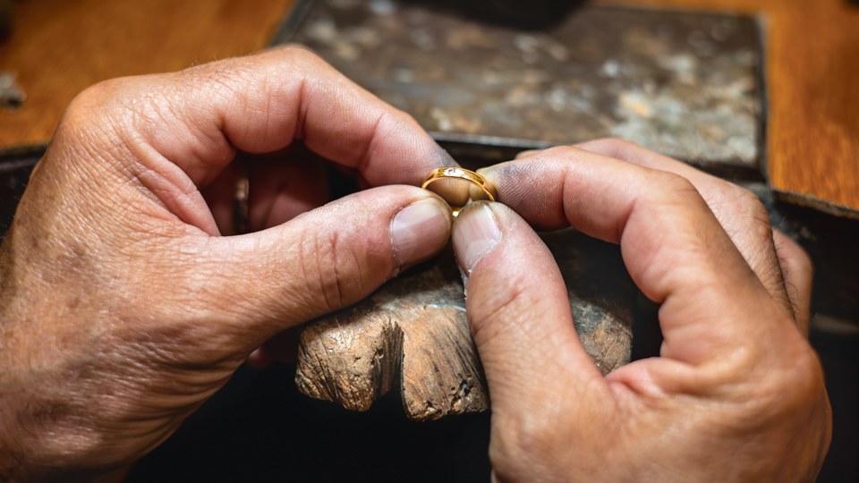 Männerhände halten einen Goldring zwischen Daumen und Zeigefingern