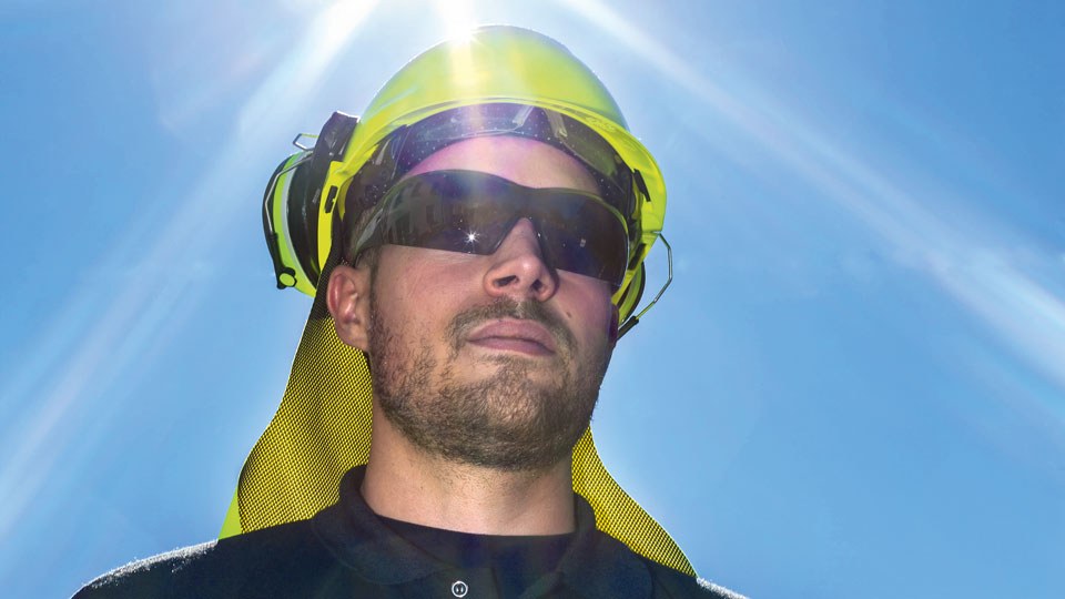 Der Oberkörper eines Mannes mit Sonnenbrille, Schutzhelm und Nackenschutz. Am Himmel scheint die Sonne.